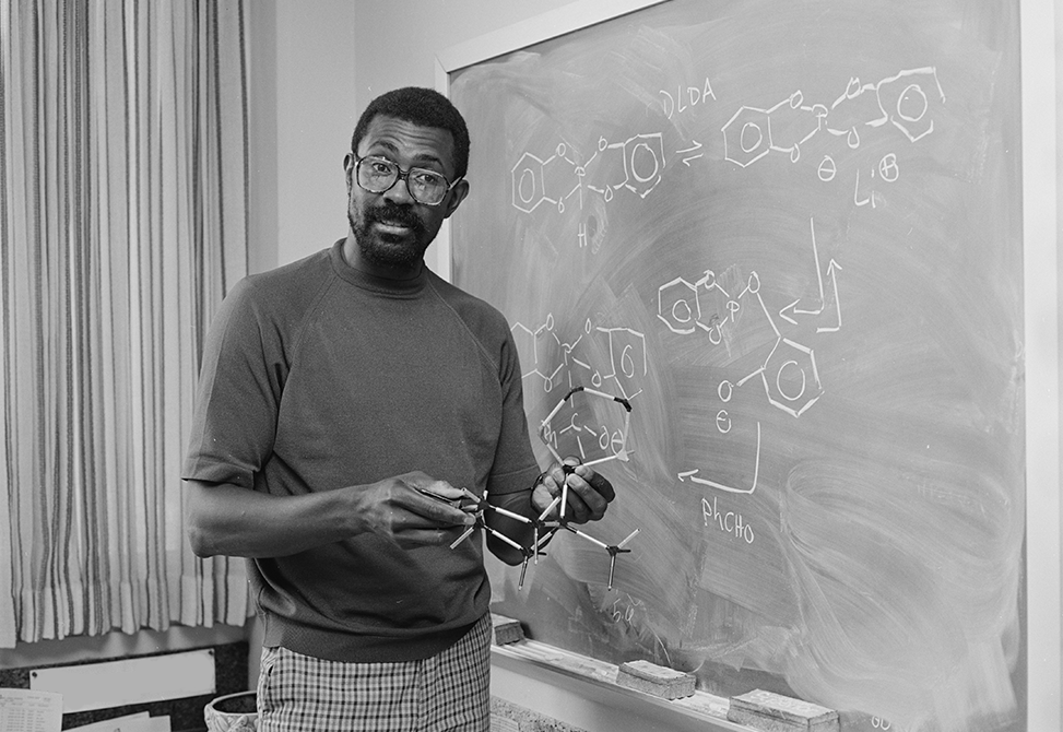 Professor Slayton Evans standing in front of a chalkboard holding a chemistry model