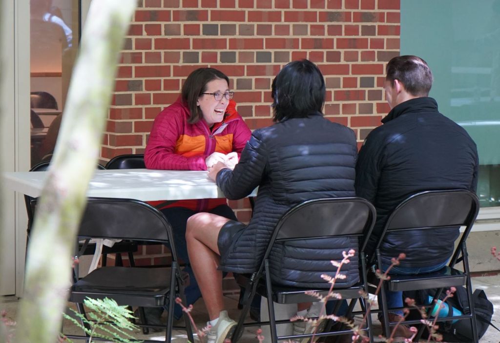 Professor Dempsey laughs while she sits at a table with two students.