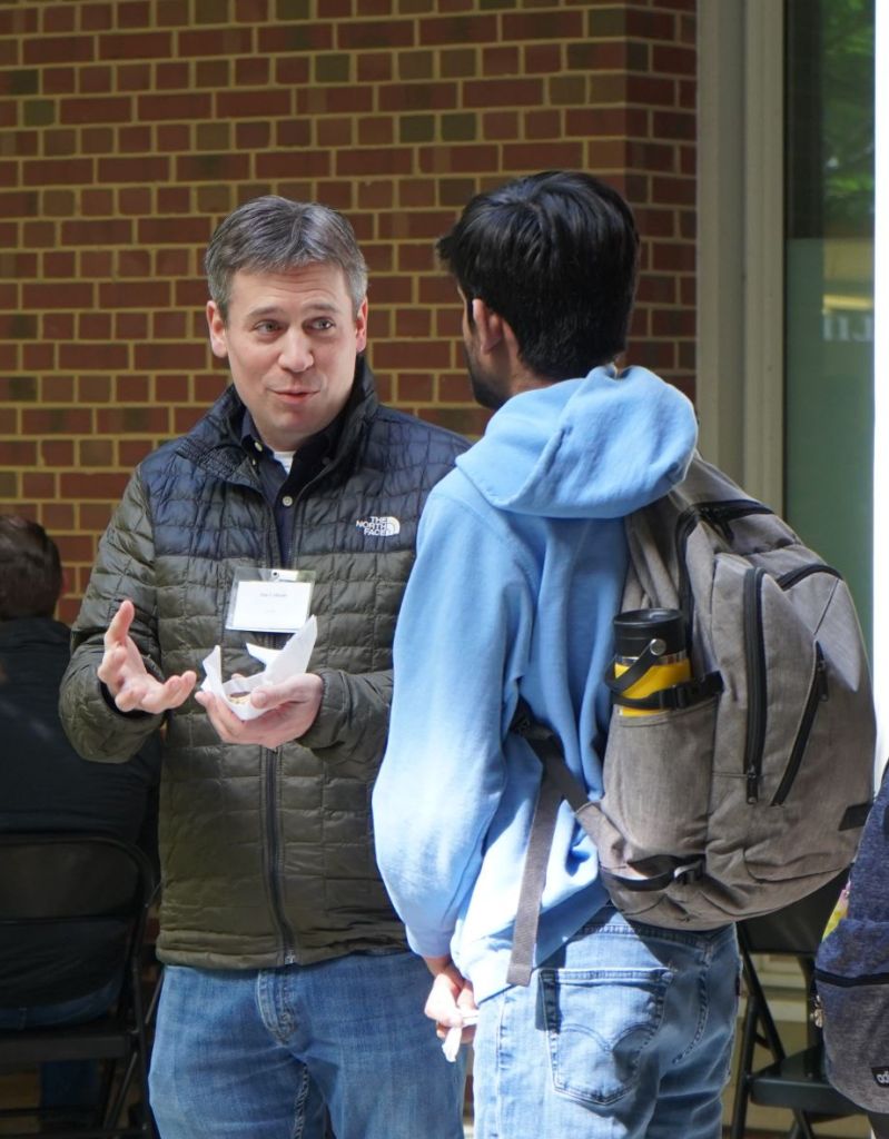 Professor Cahoon smiles at a student while he explains research. He has a cookie on a napkin in his hand.