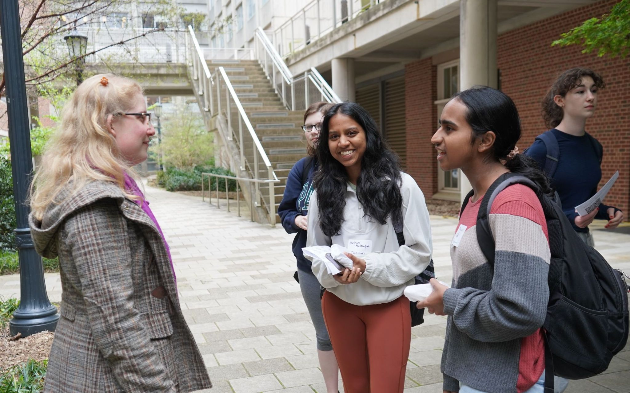 Professor Curtis talks with three students.  The student in the middle has noticed the camera and she is smiling at the photographer.