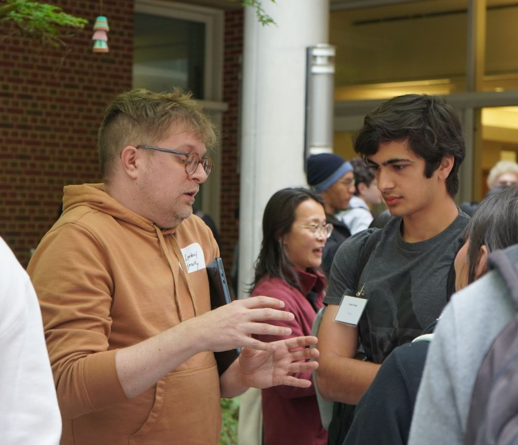 Professor Lockett discusses his research with students. In the background, Professors Li and Wilkerson-Hill can also be seen talking to students.